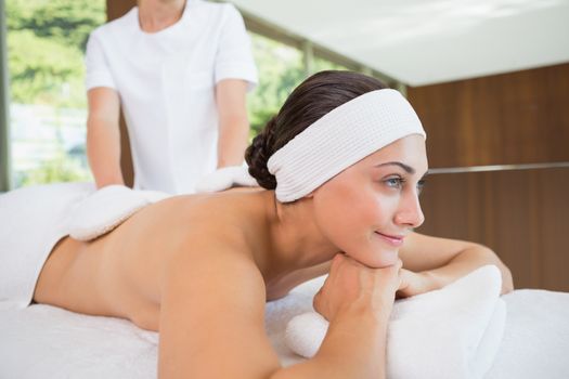 Beauty therapist rubbing smiling womans back with heated mitts in the health spa