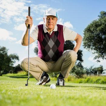 Golfer kneeling watching gold ball on a sunny day at the golf course