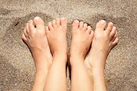 Feet of mother with daughter relaxing and sunbathing on a beach