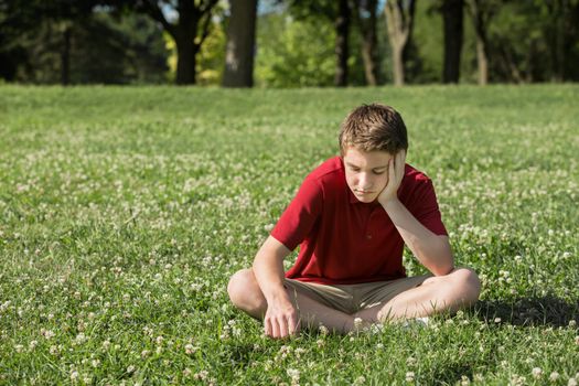 Sad young Caucasian male sitting on grass