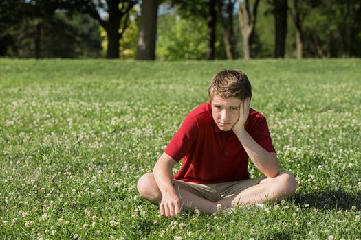 Single bored teen boy sitting on grass