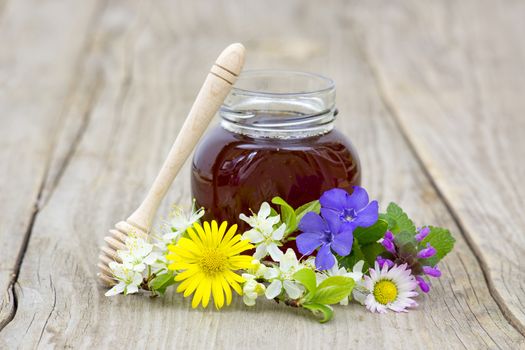 Honey in a jar and flowers on wooden background