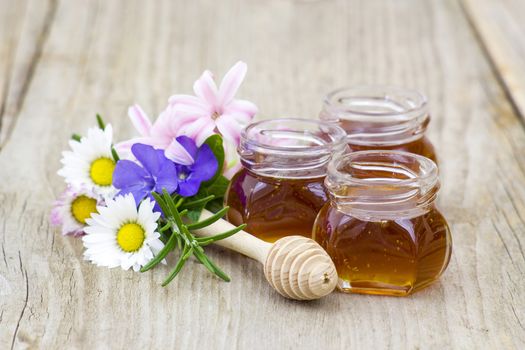 Honey in jars, flowers and honey dipper on wooden background