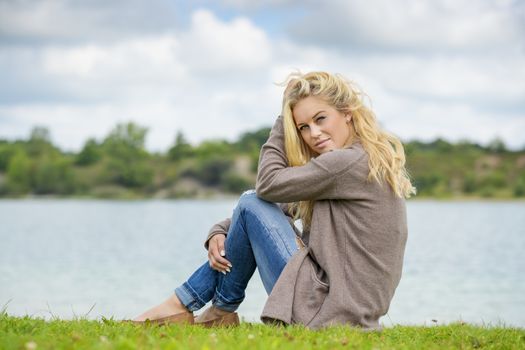 Blond woman sitting at the edge of a lake in summer