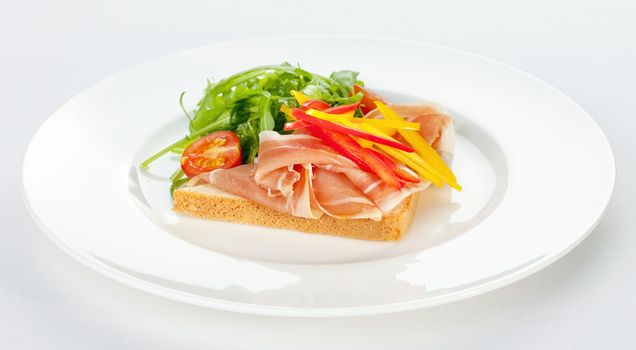 sandwich with ham, tomatoes, paprika and ruccola on a white plate