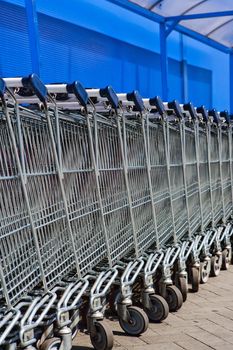 a line of empty supermarket shopping carts against blue wall