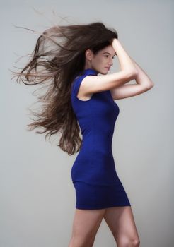 beautiful woman in blue dress with long brown hair flying - isolated on gray