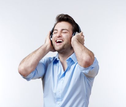 man in blue shirt with earphones listening to music - isolated on gray