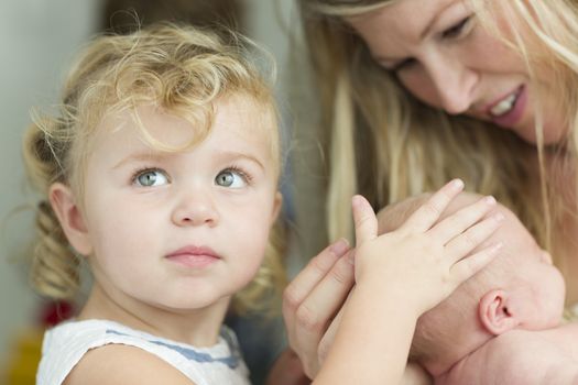 Beautiful Young Mother Holds Newborn Baby Girl as Young Sister Looks On.