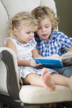 Cute Young Brother and Sister Reading a Book Together in a Chair.