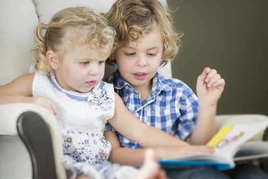 Cute Young Brother and Sister Reading a Book Together in a Chair.