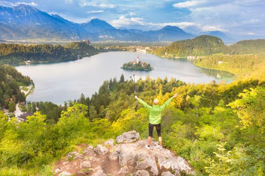 Made it. Young spoty active lady with hiking sticks and hands rised admiring beautiful nature around Bled Lake in Julian Alps, Slovenia. 