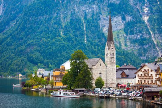 Hallstatt, Austria - August 8, 2013: View of Hallstatt village with Christuskirche church bell tower on lake shore and Alps behind, Austria