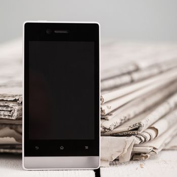 Pile of black and white newspapers with a black smartphone on a wooden table