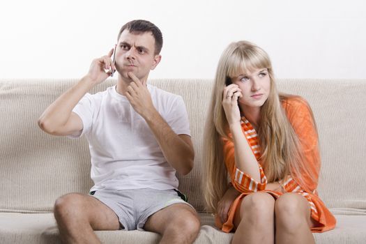 Young couple sitting on the couch. Both talk on the phone. He is very surprised to hear, girl concerned. The pair dressed home