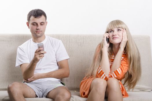 Young couple sitting on the couch. Girl on the phone. The guy writes SMS. The pair dressed home
