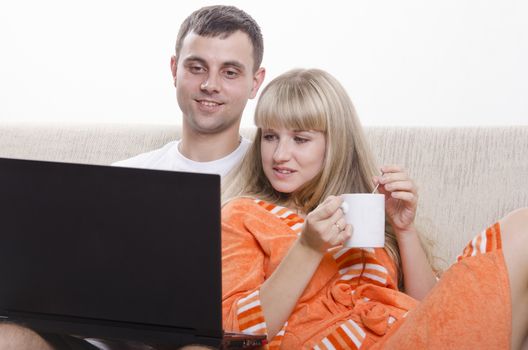 A boy and a girl sitting on the couch. A guy sitting with a laptop, a girl clung to him a Cup of tea.
