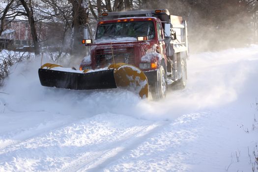 A snowplow truck removing snow from a tree lined rural road on a cold winter day.