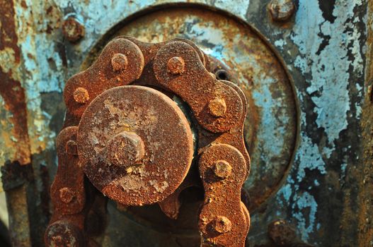 A thick chain over a sprocket rusted and weathered outside. The motor has peeling blue paint in the background.