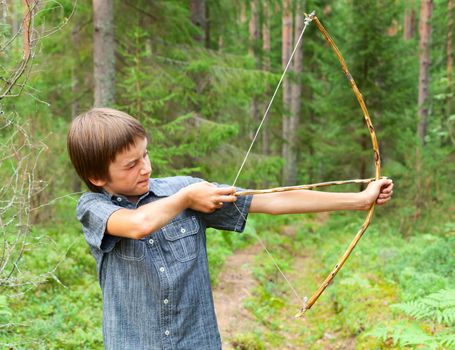 Boy aiming home-made wooden bow outdoors