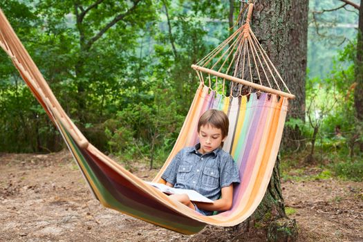 Boy lying in hammock reading a book outdoors