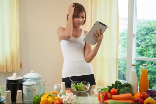 Young asian woman In Kitchen Following Recipe On Digital Tablet