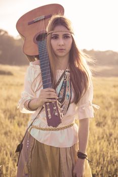 Hippie woman walking in golden field with acoustic guitar