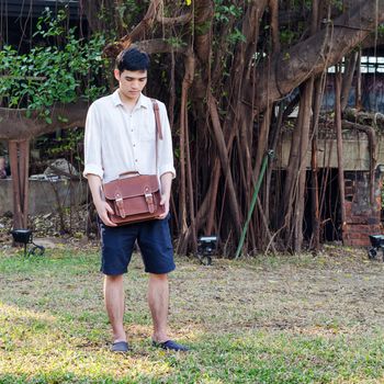 Fashionable young man with leather bag, Banyan tree background