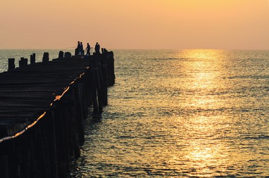 Silhouette fisherman on the old wooden bridge and sea at sunrise in rural Thailand.