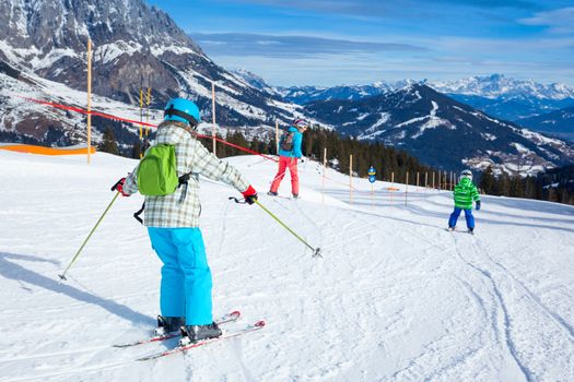 Ski, winter, snow, skiers, sun and fun - Back view of two happy kids with mother enjoying winter vacations.