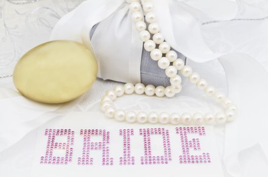 Feminine image of wedding day financial savings start.  Gold nest egg placed with BRIDE in pink letters surrounded by white ribbon, gray velvet gift box, and pearl necklace. 