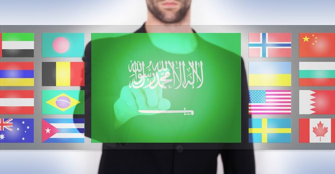 Hand pushing on a touch screen interface, choosing language or country, Saudi Arabia