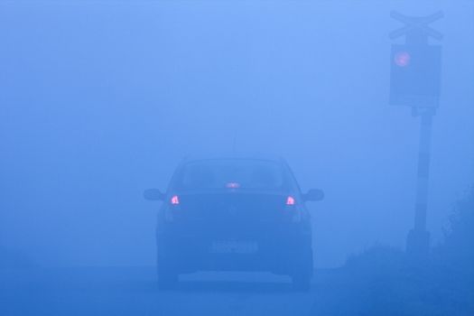 car waiting at rural railroad crossing with red lights blinking in fog