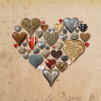 Photo of heart-shaped things made of stone, metal and wood organized in the shape of a heart over vintage paper background.