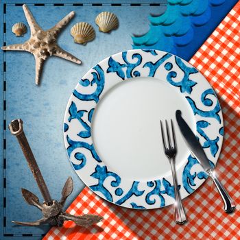 Empty plate with fork and knife, red and white checkered tablecloth, seashells, starfish, blue waves and rusty anchor. Table set for a seafood menu