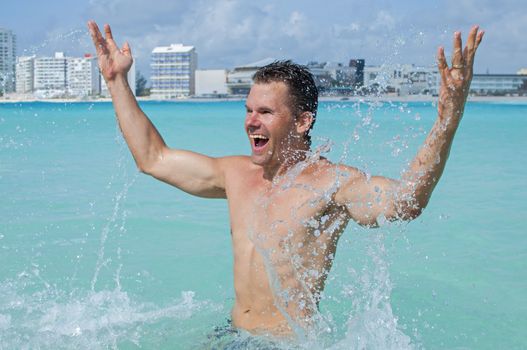 Young fit and shirtless Caucasian man celebrates by splashing in shallow tropical waters of beautiful beach resort