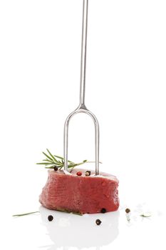 Raw filet mignon on fork steak with herbs and peppercorns isolated on white background. Luxurious red meat steak eating. 