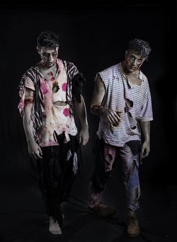 Two male zombies standing on black background walking towards camera