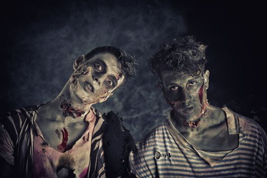 Two male zombies standing on black smoky background, head and shoulder shot
