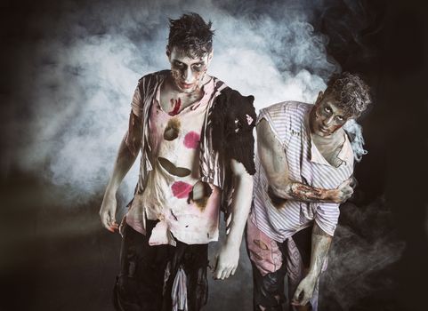 Two male zombies standing on black smoky background, looking at camera