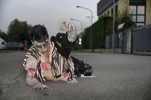 Male zombie crawling on his knees, on empty city street, looking at camera reaching out one hand. Halloween theme