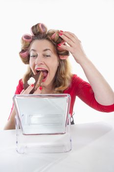 middle-aged woman with hair rollers eating cake looking at mirror