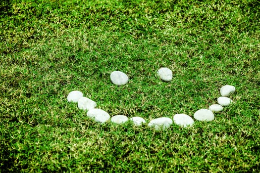 arranging white stone on the green grass in smile concept for eco background