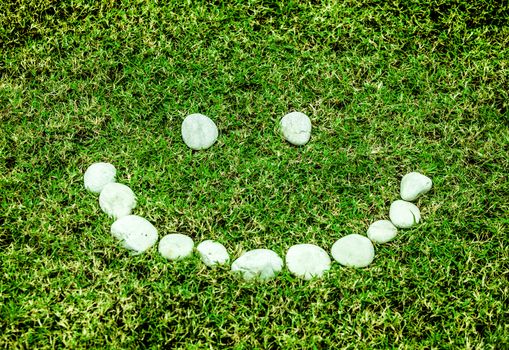 arranging white stone on the green grass in smile concept for eco background