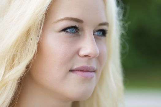 Outdoor portrait of a young blond woman in summer with green background