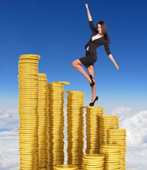 Businesswoman climbing stairs of gold coins. Sky and clouds in background