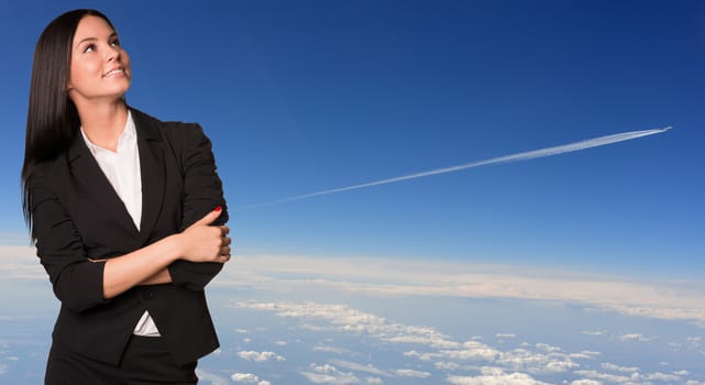 Businesswoman smiling and looking up. Blue sky with plane race as backdrop