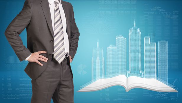 Businessman in suit standing and holding hands on hips. Glowing wire-frame buildings on open empty book as backdrop