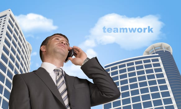 Businessman talking on the phone. Skyscrapers and cloud with word teamwork in background