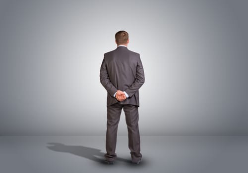 Businessman in suit standing in an empty gray room. Rear view